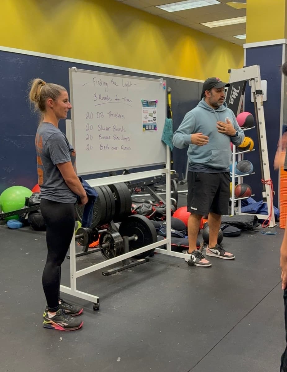 Two people at the gym beside a whiteboard showing the Finding the Light workout