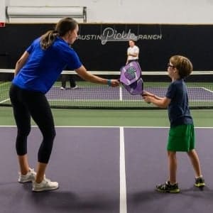 A woman teaching a young boy to play pickleball